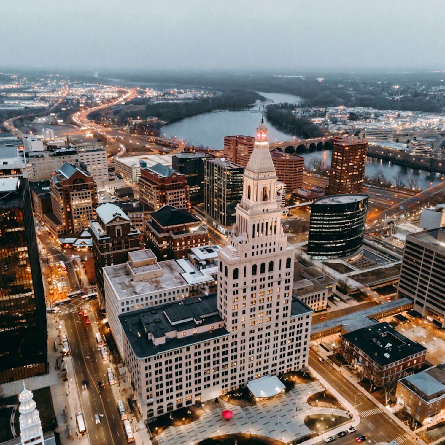 Aerial view of a cityscape at dusk with illuminated buildings and roads.