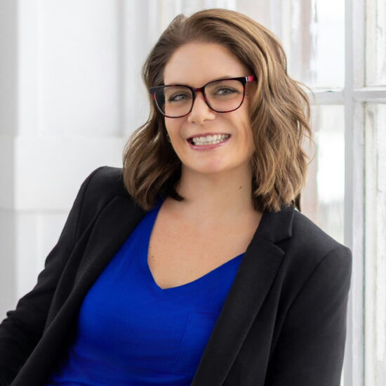 Smiling woman in blue shirt and blazer, sitting by window.