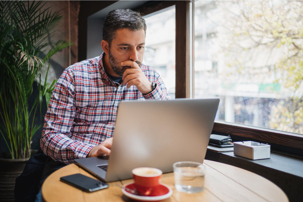 man on laptop sitting by window in a cafe