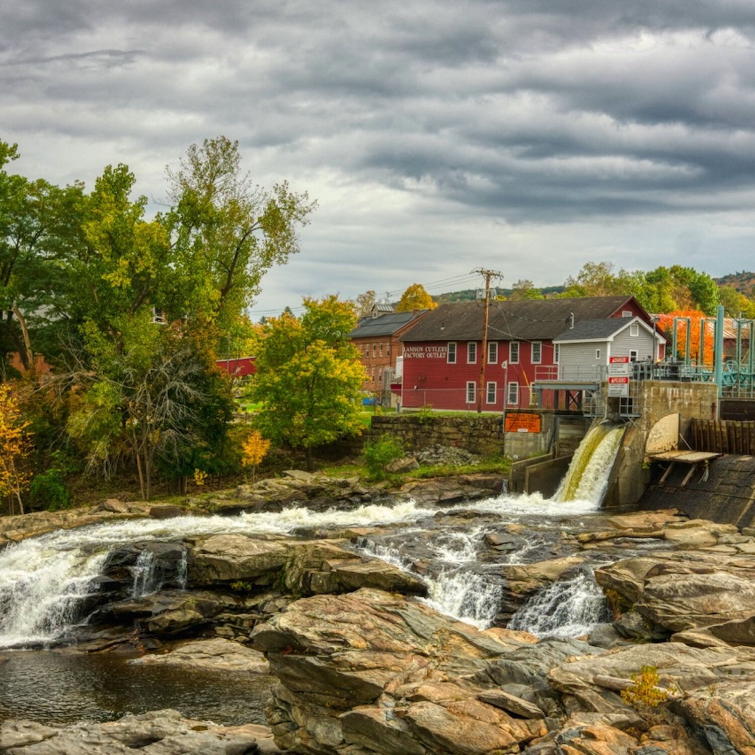 Scenic view of a river and dam with autumn foliage and cloudy sky.