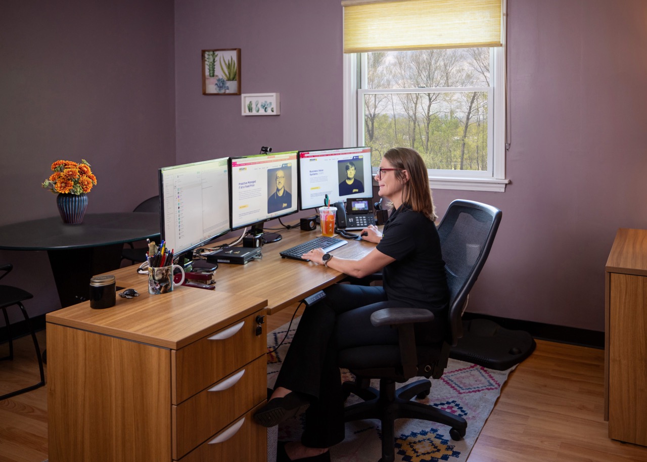 A woman working at a desk with dual monitors in a home office.