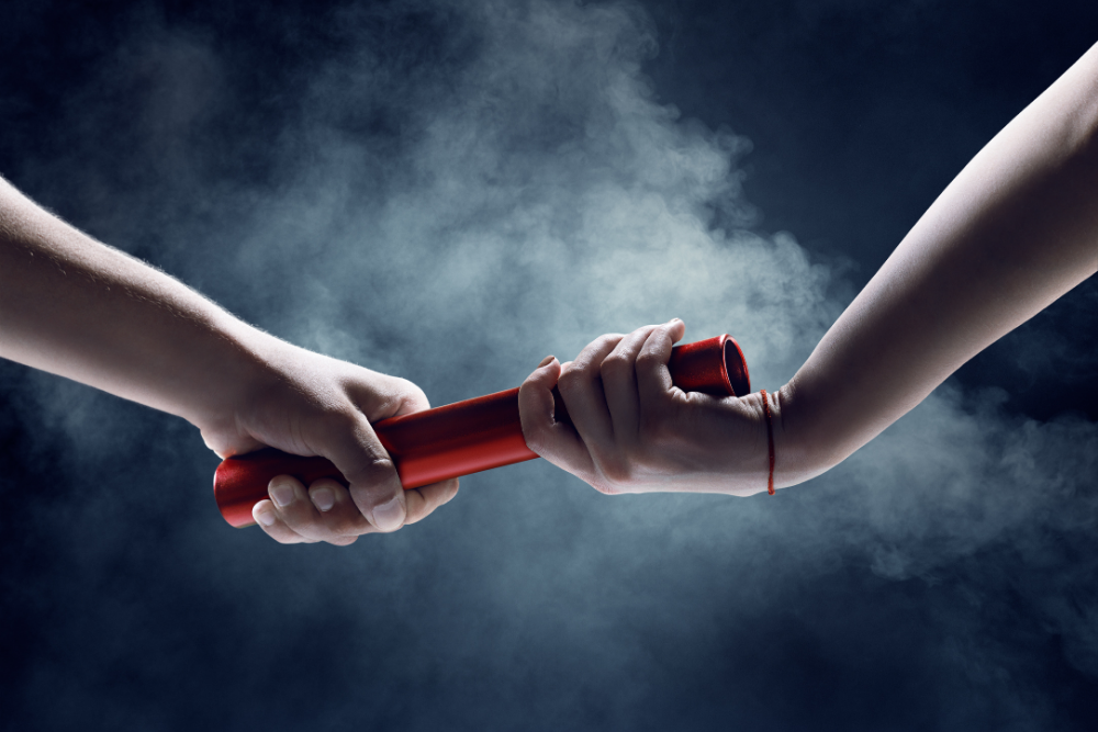 Hands passing a red baton in a smoky atmosphere, symbolizing teamwork and connection.